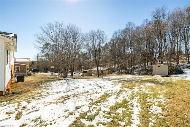 yard layered in snow with central AC and a storage shed