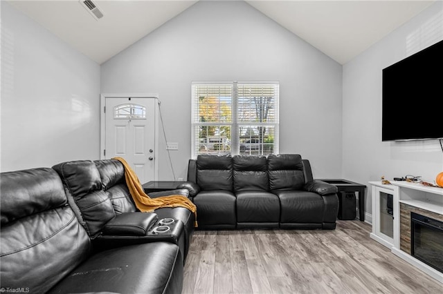 living room featuring high vaulted ceiling, light hardwood / wood-style flooring, and a stone fireplace