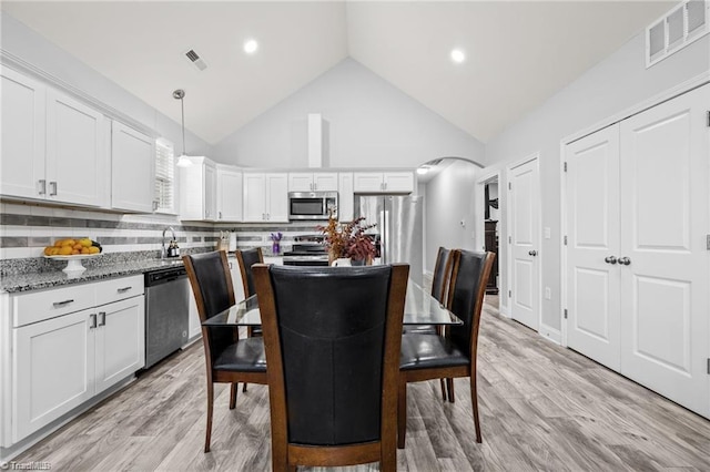 dining room with high vaulted ceiling and light hardwood / wood-style flooring