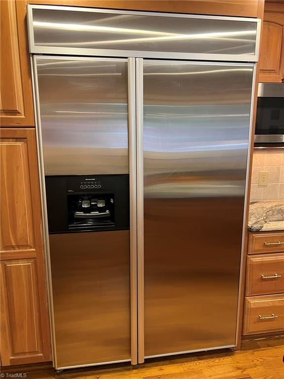 590 Knob View Dr, Winston-Salem, NC 27104 - detailed view of stainless steel appliances, light wood-style floors, brown cabinets, light stone countertops, and decorative backsplash