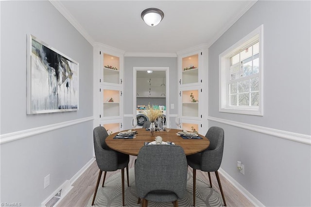 dining area featuring built in shelves, crown molding, and light wood-type flooring