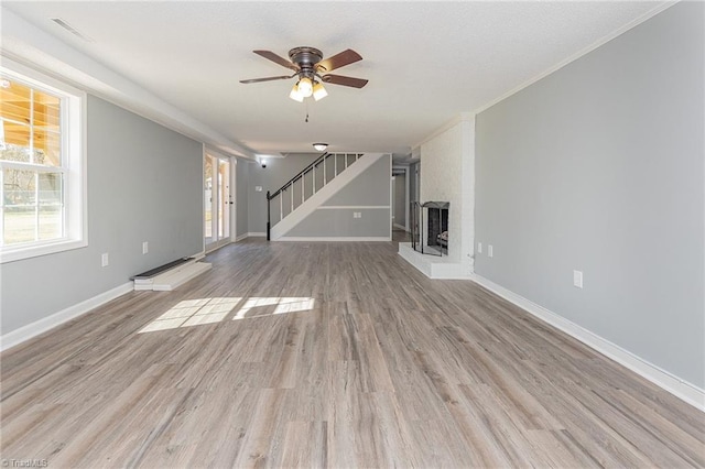 unfurnished living room featuring ceiling fan, ornamental molding, a fireplace, and light hardwood / wood-style flooring