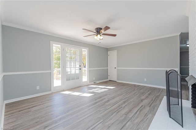 spare room featuring light hardwood / wood-style floors, a brick fireplace, ceiling fan, and crown molding