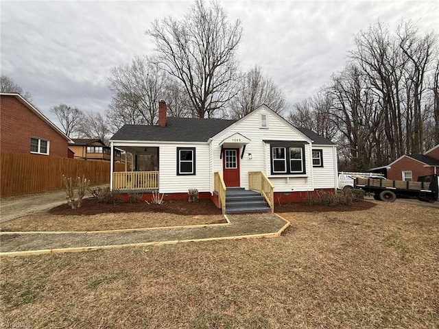 bungalow-style home featuring a front lawn, a chimney, roof with shingles, and fence