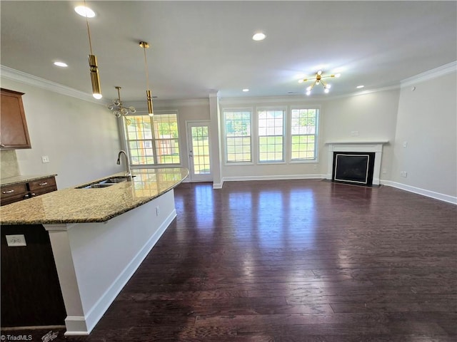 kitchen featuring sink, dark wood-type flooring, light stone counters, pendant lighting, and a center island with sink