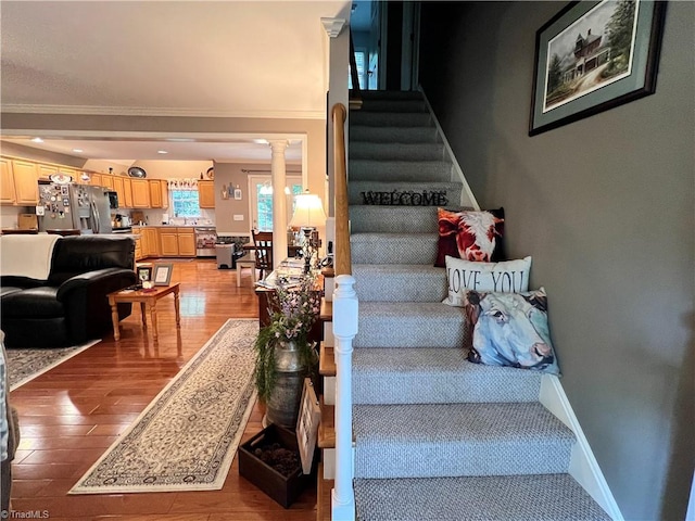 stairway featuring hardwood / wood-style floors, crown molding, and ornate columns