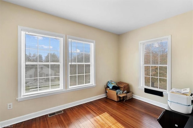 empty room featuring wood-type flooring, visible vents, baseboards, and a healthy amount of sunlight