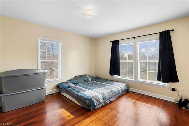 bedroom with multiple windows, wood-type flooring, and baseboards