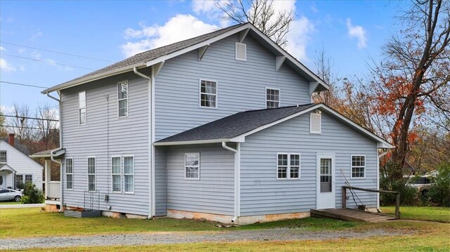 back of property with a shingled roof and a yard