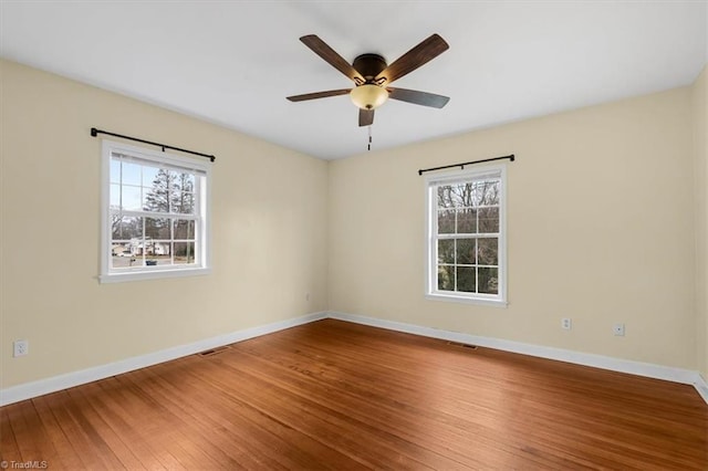 spare room with a ceiling fan, visible vents, baseboards, and hardwood / wood-style floors