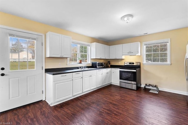 kitchen with dark wood-style flooring, dark countertops, appliances with stainless steel finishes, white cabinetry, and under cabinet range hood