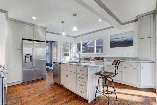 kitchen with appliances with stainless steel finishes, light stone counters, sink, decorative light fixtures, and hardwood / wood-style flooring