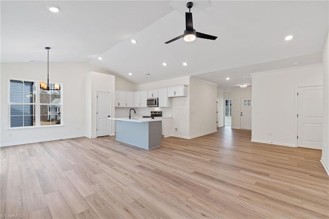 unfurnished living room featuring ceiling fan with notable chandelier, vaulted ceiling, sink, and light hardwood / wood-style flooring