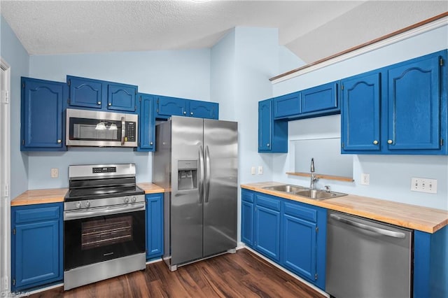 kitchen with wooden counters, a sink, blue cabinetry, stainless steel appliances, and lofted ceiling