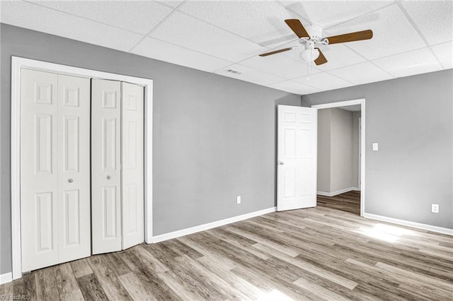 unfurnished bedroom with a paneled ceiling, ceiling fan, a closet, and light wood-type flooring