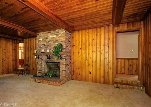 unfurnished living room featuring carpet floors, beamed ceiling, a brick fireplace, and wood ceiling