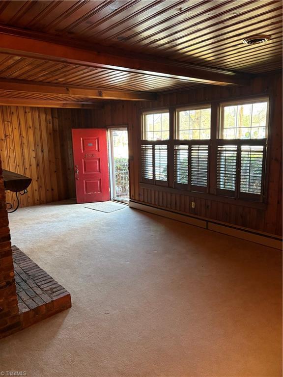 foyer with carpet floors, a baseboard heating unit, beamed ceiling, and wooden walls