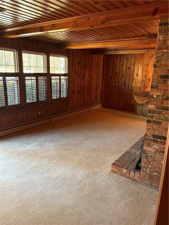 unfurnished living room with carpet flooring, wooden ceiling, a baseboard heating unit, wooden walls, and beam ceiling