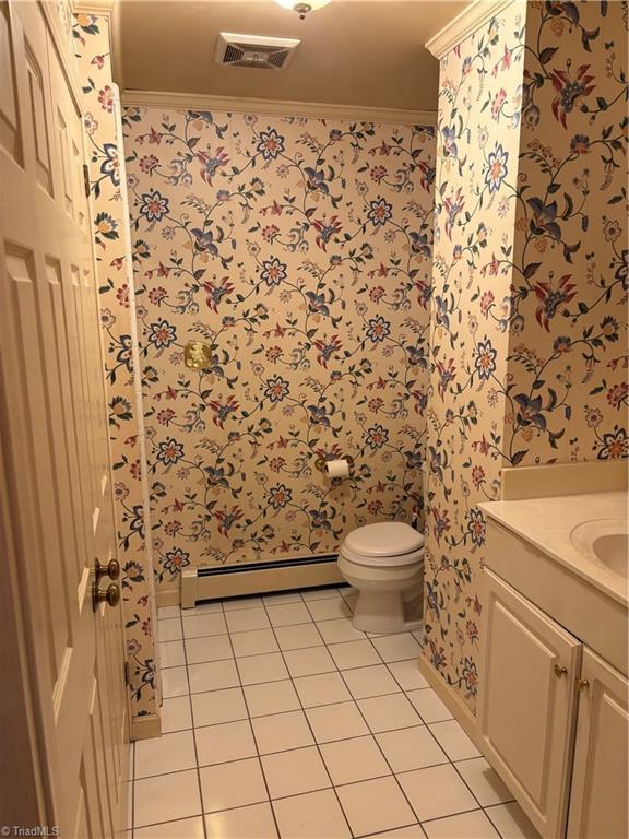 bathroom with tile patterned flooring, a baseboard heating unit, vanity, toilet, and crown molding