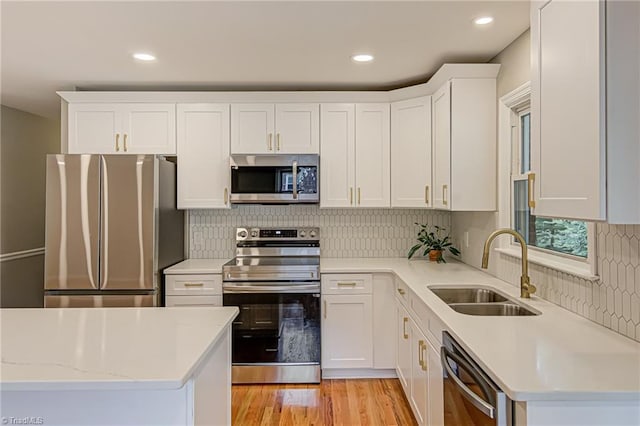 kitchen with sink, appliances with stainless steel finishes, white cabinets, decorative backsplash, and light wood-type flooring