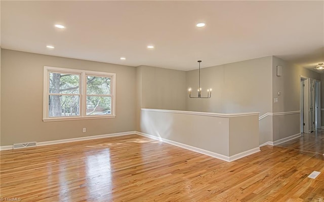 spare room with an inviting chandelier and light hardwood / wood-style flooring