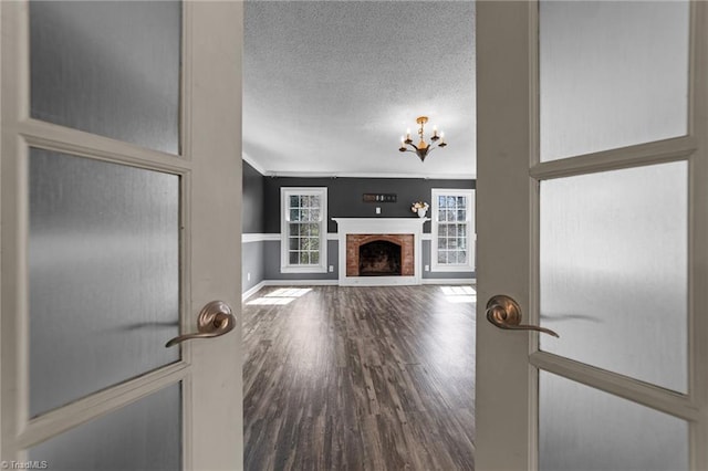 unfurnished living room featuring wood finished floors, an inviting chandelier, crown molding, a textured ceiling, and a fireplace