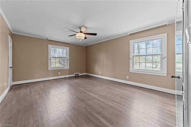 empty room with baseboards, visible vents, ceiling fan, wood finished floors, and crown molding