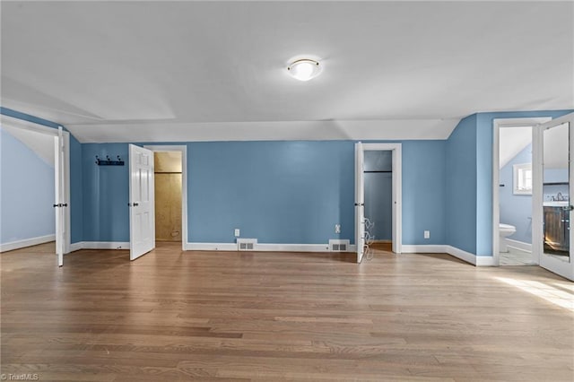 unfurnished bedroom featuring vaulted ceiling, wood finished floors, visible vents, and baseboards