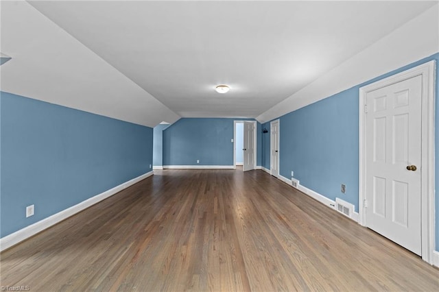 additional living space with lofted ceiling, visible vents, baseboards, and wood finished floors