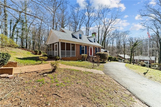 view of property exterior featuring aphalt driveway, a sunroom, brick siding, and a yard