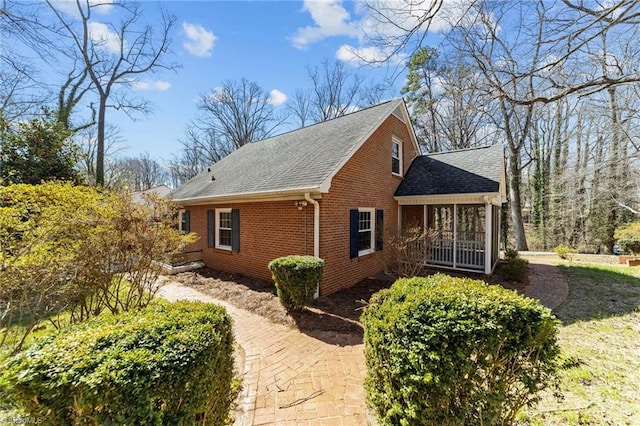 view of side of home with a shingled roof and brick siding