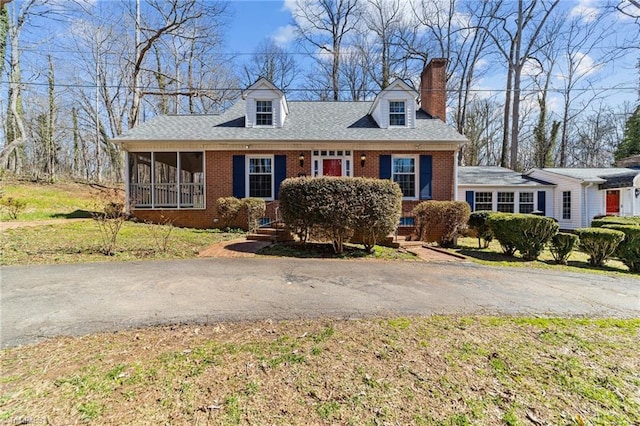 new england style home featuring brick siding, a chimney, and a sunroom