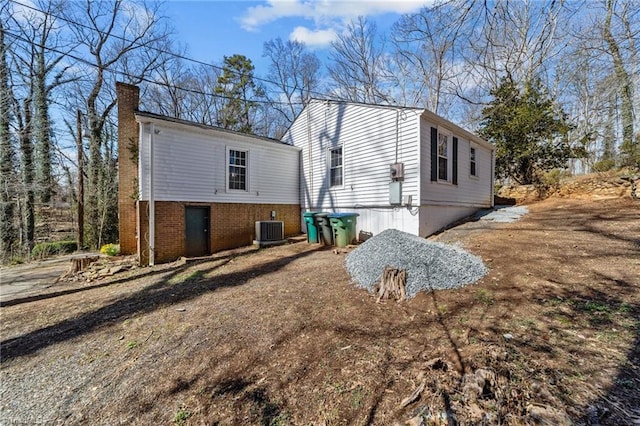 view of home's exterior with central AC, brick siding, and a chimney