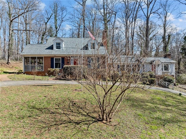 cape cod home with a sunroom, brick siding, a front lawn, and roof with shingles