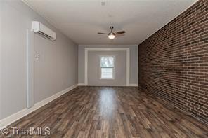 interior space with a wall unit AC, a ceiling fan, wood finished floors, brick wall, and baseboards