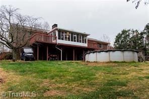 rear view of property featuring an outdoor pool, a deck, and a yard