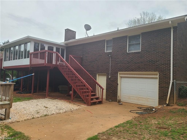 rear view of property featuring a sunroom, an attached garage, a chimney, stairway, and brick siding