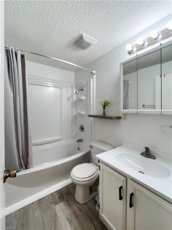 full bathroom featuring hardwood / wood-style floors, vanity, shower / tub combo, toilet, and a textured ceiling