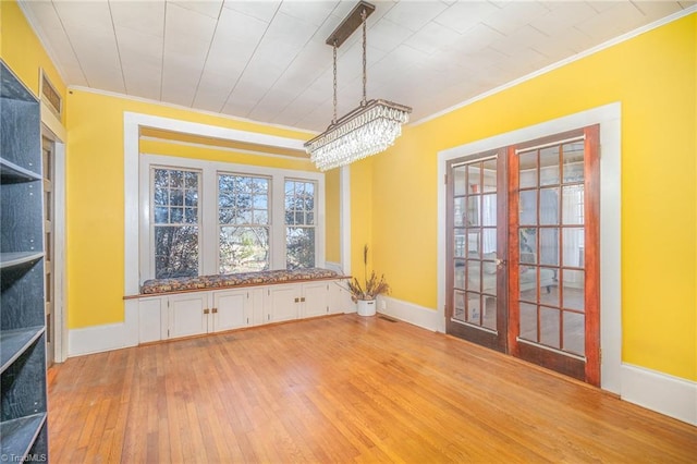 unfurnished dining area with light wood-style flooring, a notable chandelier, baseboards, and ornamental molding