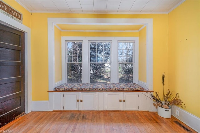 interior space with visible vents, baseboards, wood finished floors, and ornamental molding