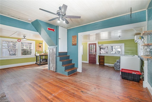 living room with stairway, a wall mounted AC, ceiling fan, and hardwood / wood-style floors