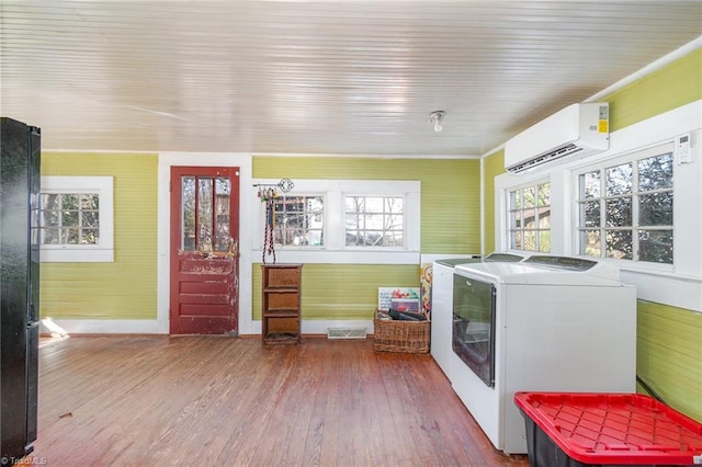 laundry area with visible vents, separate washer and dryer, wood finished floors, and a wall unit AC