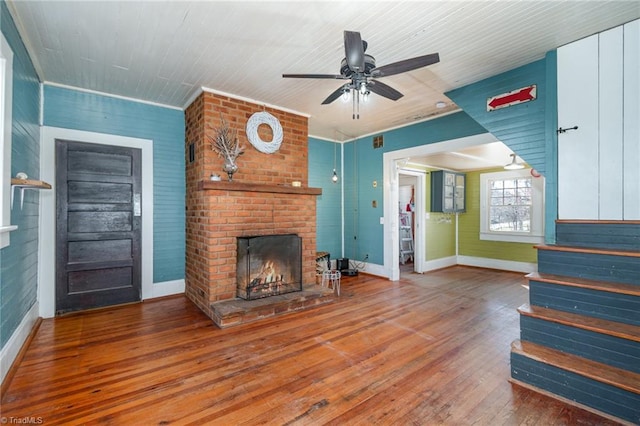 unfurnished living room featuring baseboards, ceiling fan, stairway, a fireplace, and hardwood / wood-style flooring