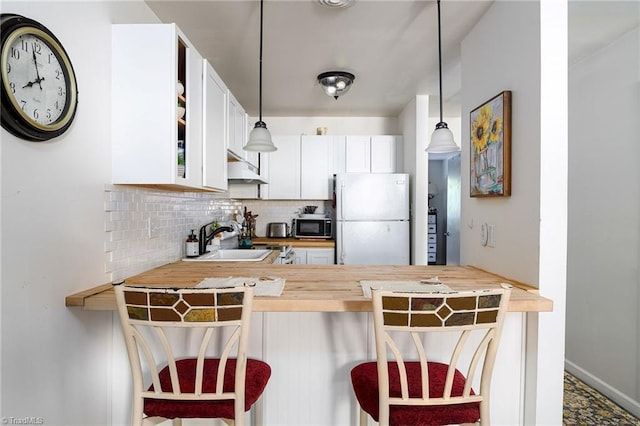 kitchen featuring freestanding refrigerator, decorative backsplash, a peninsula, a sink, and decorative light fixtures
