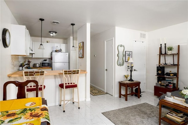 kitchen featuring marble finish floor, freestanding refrigerator, a peninsula, decorative light fixtures, and decorative backsplash