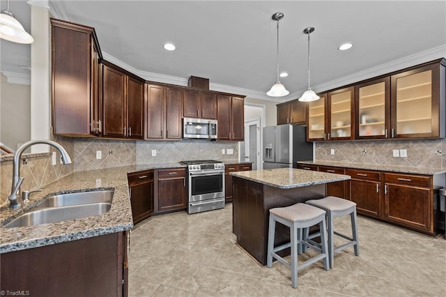 kitchen with a kitchen island, sink, hanging light fixtures, stainless steel appliances, and light stone countertops