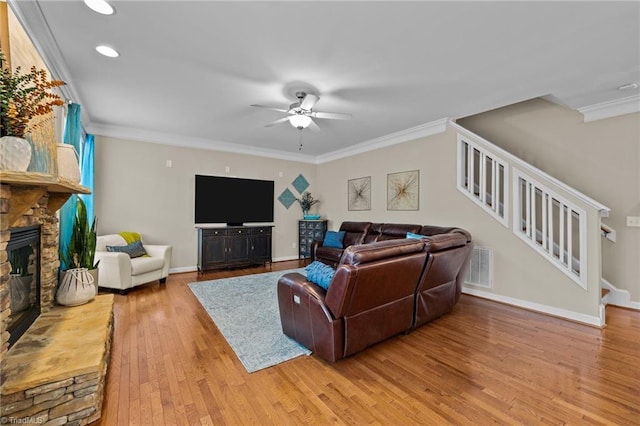 living room with crown molding, ceiling fan, a stone fireplace, and light hardwood / wood-style flooring