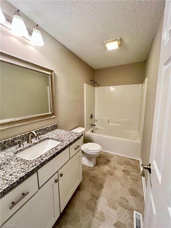 full bath featuring shower / tub combination, toilet, vanity, and a textured ceiling