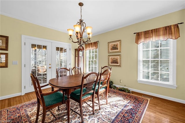 dining space with an inviting chandelier, light wood-style flooring, ornamental molding, and french doors