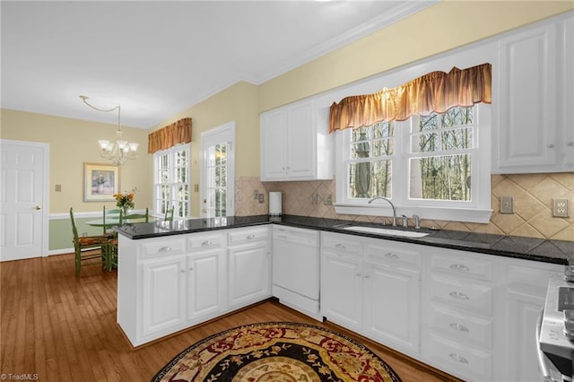 kitchen featuring white cabinets, dishwasher, dark countertops, a peninsula, and a sink